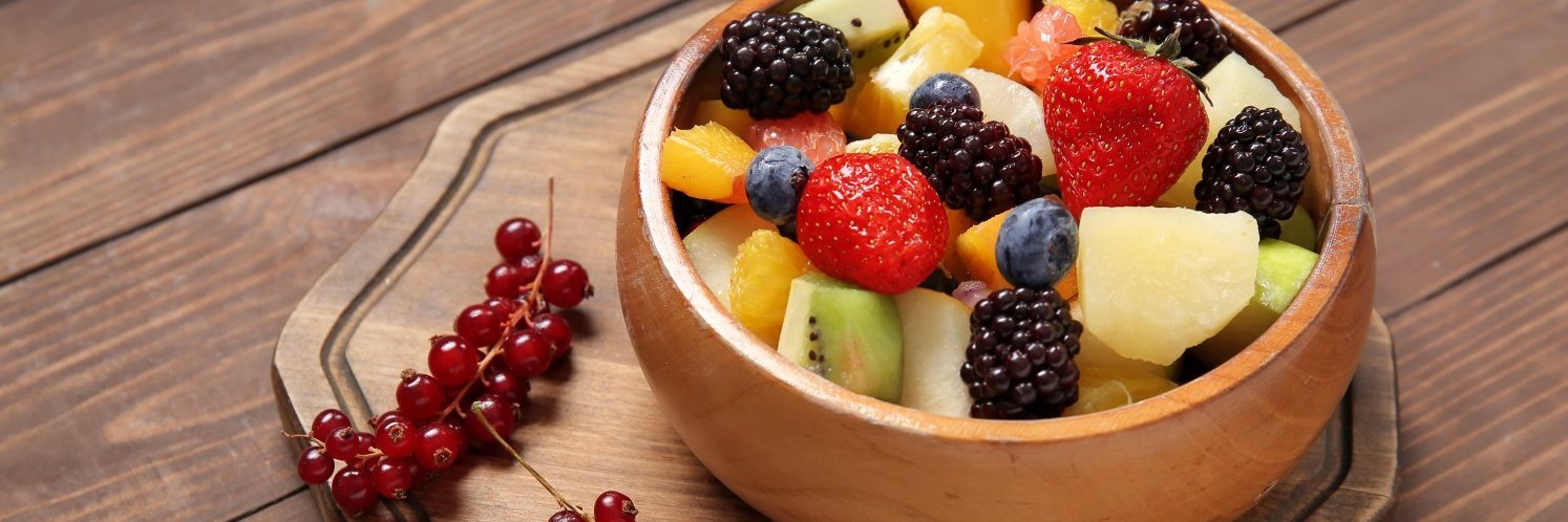 Ein bunter Obstsalat mit Erdbeeren, Brombeeren, Heidelbeeren, Apfel und Johannisbeeren in einer Holzschüssel. 