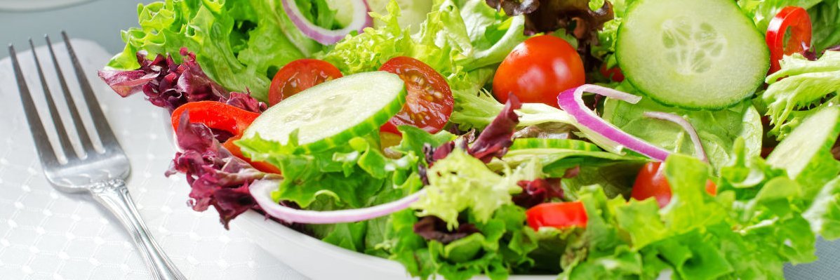 Neben einer Schuessel mit buntem Salat liegt eine Gabel.