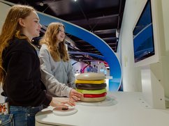 Zwei Jugendliche stehen an einem Ausstellungsexponat, der einen Hamburger darstellt.