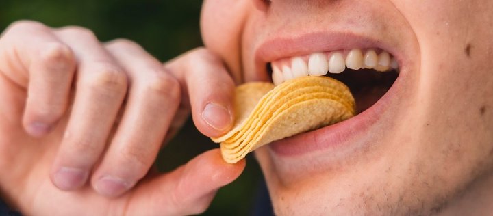 Auf dem Bild ist dargestellt, wie mehrere Kartoffelchips mit der Hand in den Mund gesteckt werden. 