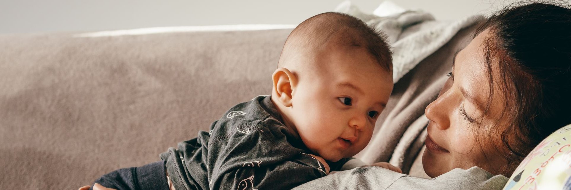 Eine Mutter und Ihr Baby liegen auf der Couch und kuscheln.