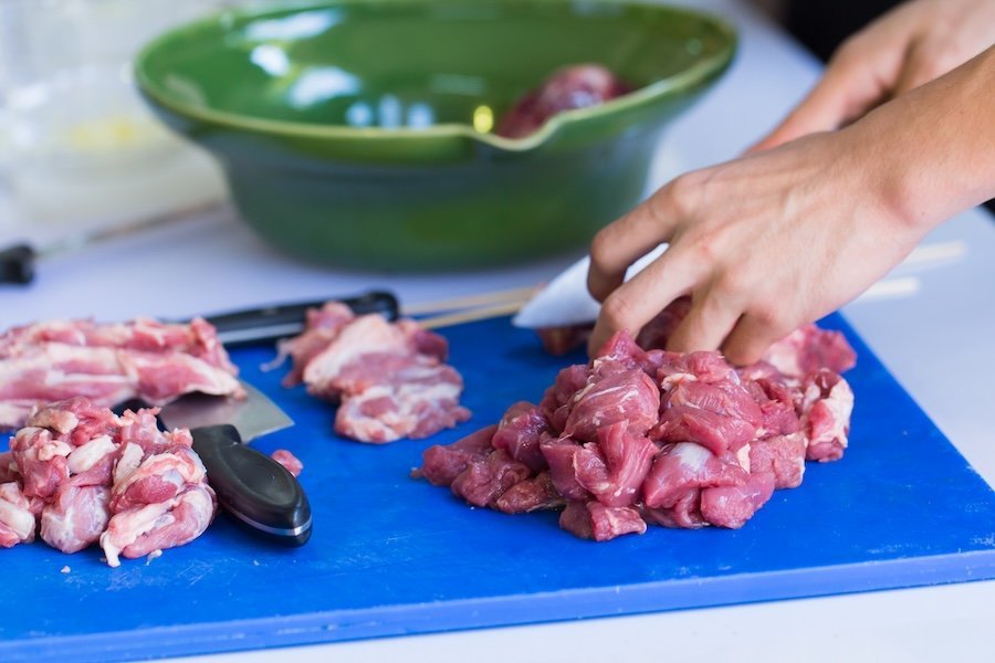 Haende schneiden Fleisch hygienisch auf einem Brettchen.
