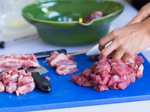 Haende schneiden Fleisch hygienisch auf einem Brettchen.