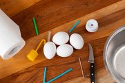 Vier Eier liegen auf dem Tisch, umrahmt von Messer, Zahnstocher, Strohhalm und anderen Utensilien.