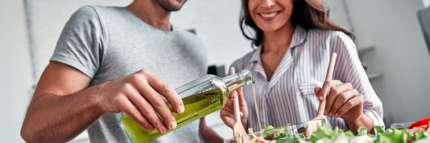 Junger Mann gießt Öl in eine Salatschüssel.