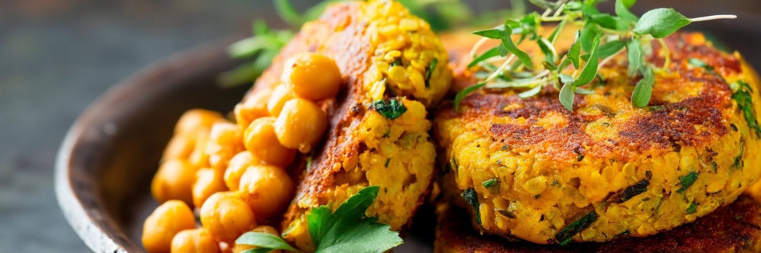 Kichererbsen liegen neben Bratlingen in einer braunen Schale.