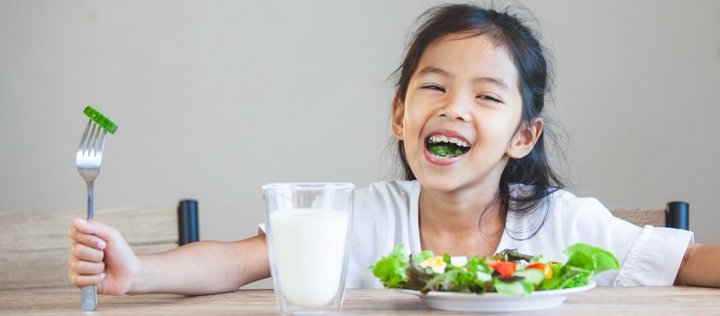 Mädchen lacht vor Gemüseteller und Glas Milch