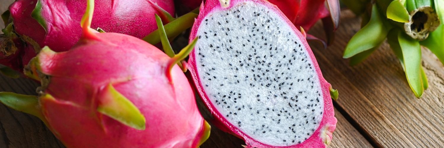 Mehrere ganze und eine halbierte Pitaya liegen auf einem dunklen Holzuntergrund.