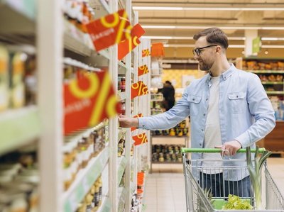 Ein Mann mit einem Einkaufswagen steht im Supermarkt vor einem Regal mit Angeboten.