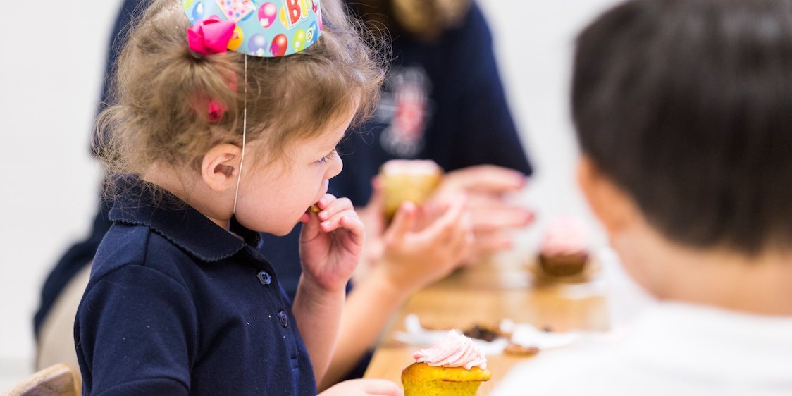 Ein Kleinkind mit Geburtstagshütchen isst einen süßen Muffin.. Artikel "Umgang mit Zucker in der KiTa " öffnen.