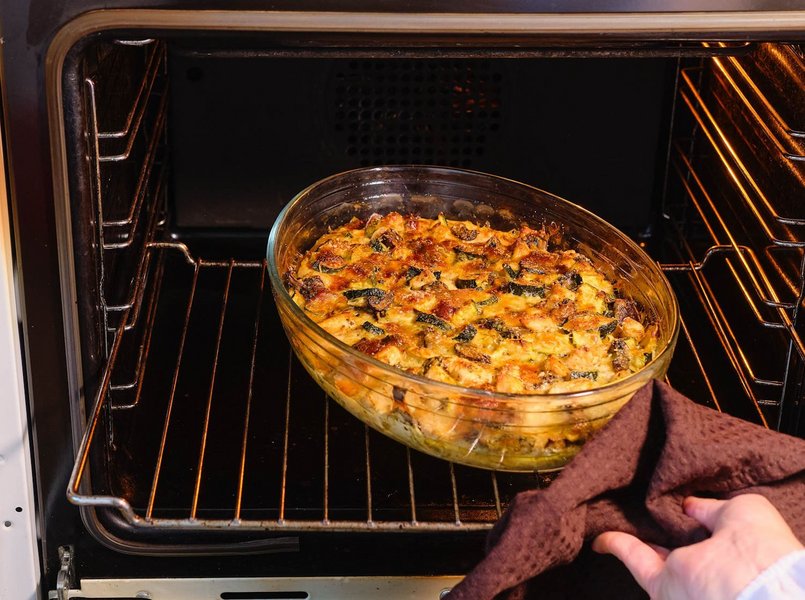 In einem geöffneten Backofen steht eine Glasschüssel mit einem fertigen Auflauf.