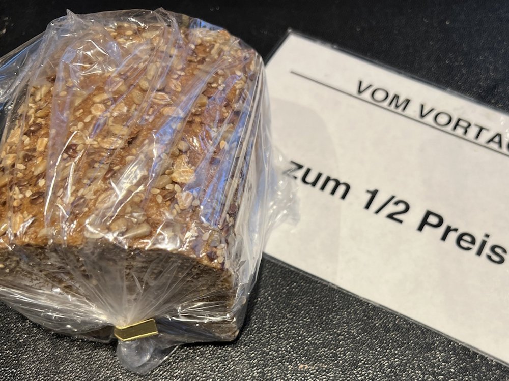 Neben einem in einer Tüte verpackten Brot liegt ein Schild mit der Aufschrift "Vom Vortag: zum 1/2 Preis".