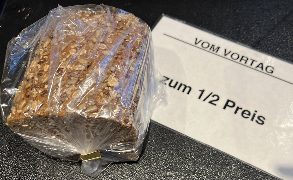 Neben einem in einer Tüte verpackten Brot liegt ein Schild mit der Aufschrift "Vom Vortag: zum 1/2 Preis".