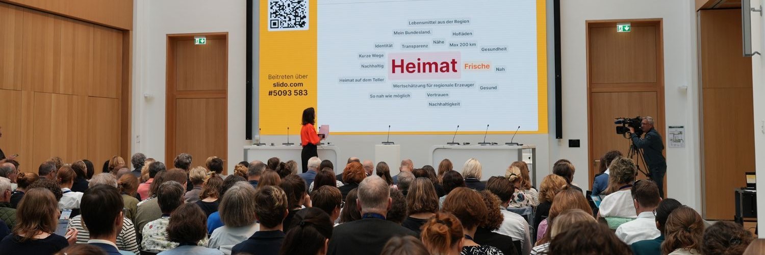 Der mit Besucherinnen und Besuchern gefüllte Veranstaltungsraum des Deutschen Ernährungstags 2026. Im Vordergrund spricht eine Referentin. Auf der Leinwand ist eine Wortwolke, in der Mitte steht das Wort Heimat.