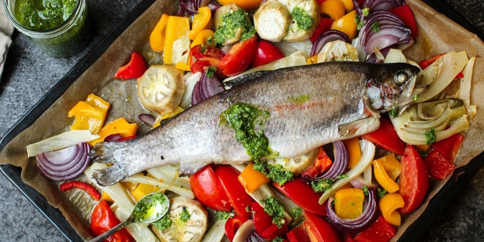 Auf einem Backblech mit buntem Gemüse liegt ein ganzer Fisch.. Artikel "Fisch und Meeresfrüchte: Gesundheit und Umwelt" öffnen.
