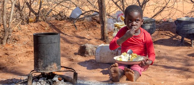 ein Kind isst an einer Feuerstelle aus einer Pfanne