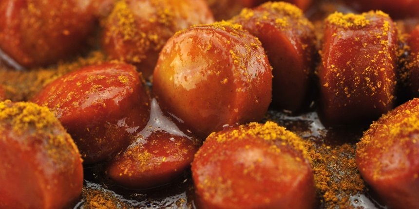 Auf einem dunklen Untergrund liegen Wurstscheiben in Sauce mit Currypulver bestäubt. . Artikel "Einfach weniger Fleisch in der Kantine" öffnen.