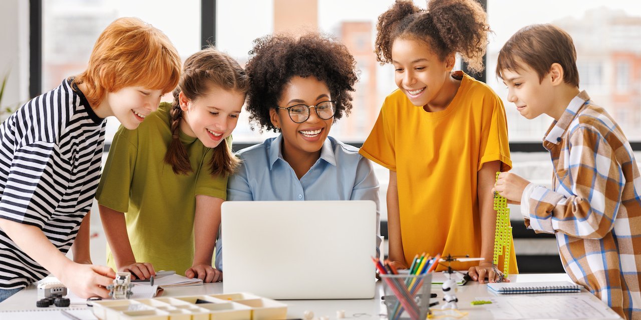 Fünf Schülerinnen und Schüler schauen gemeinsam auf einen Laptop.. Artikel "Material für die Schule" öffnen.