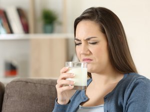 Eine Frau riecht an einem Glas mit Milch und rümpft die Nase.