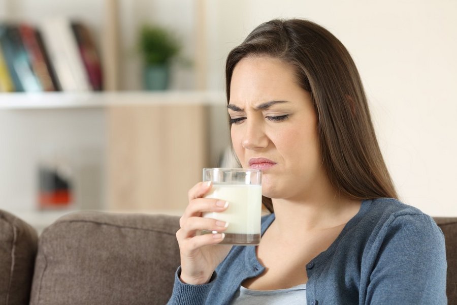 Eine Frau riecht an einem Glas mit Milch und rümpft die Nase.