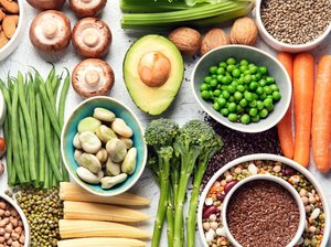 Ein Tisch ist mit verschiedenen Lebensmitteln gedeckt: Bohnen, Nüsse, Pilze, Brokkoli, Linsen, Trockenfrüchte, Mais und mehr.