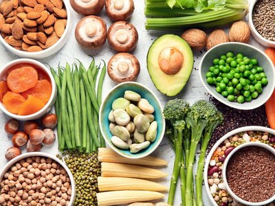 Ein Tisch ist mit verschiedenen Lebensmitteln gedeckt: Bohnen, Nüsse, Pilze, Brokkoli, Linsen, Trockenfrüchte, Mais und mehr.