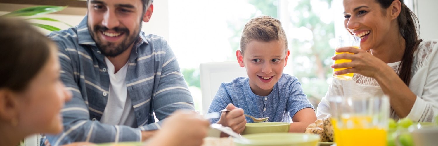 Eine junge Familie mit zwei Kindern sitzt gemeinsam am Tisch beim Frühstück und unterhält sich beim Essen.