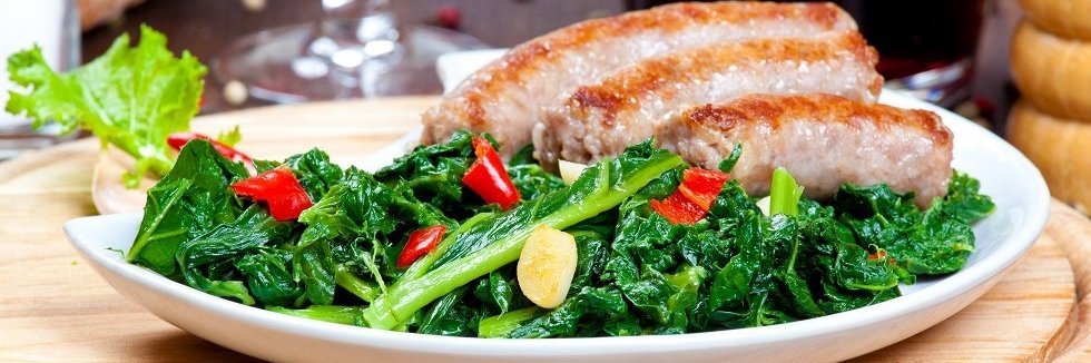 Auf einem weißen Teller liegen gekochtes Stielmus mit Knoblauch- und Chilistückchen und Bratwürste. 