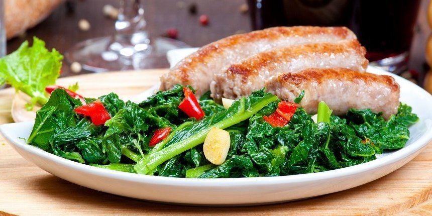 Auf einem weißen Teller liegen gekochtes Stielmus mit Knoblauch- und Chilistückchen und Bratwürste. . Artikel "Saison für Stielmus" öffnen.