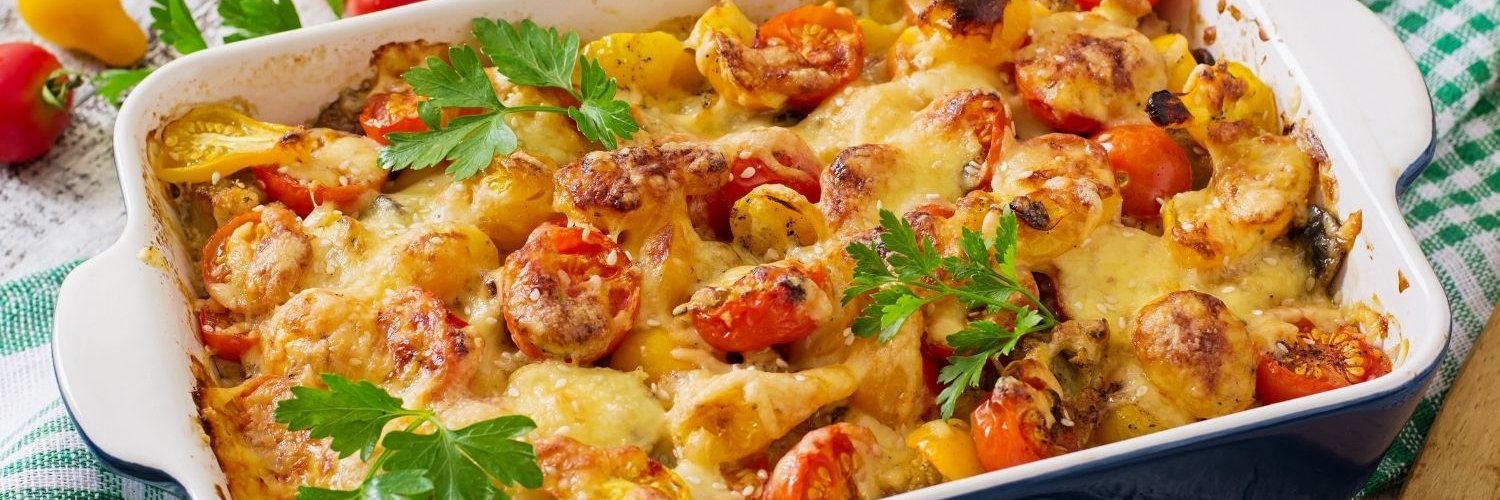 In einer weißen eckigen Auflaufform sind Tomaten, Zucchini und Pilze mit Käse überbacken und mit Petersilie dekoriert.