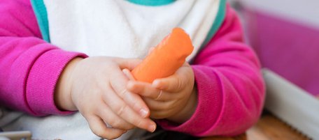 Babyhände halten eine geschälte Karotte.