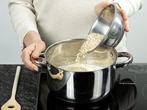 Eine Person schüttet Haferflocken in einen Topf mit Milch.