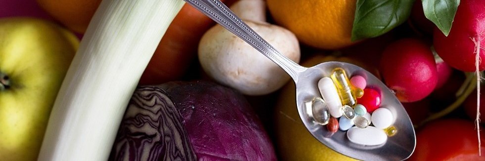 Obst und Gemüse und da drüber ein Löffel mit Nahrungsergänzungsmitteln.