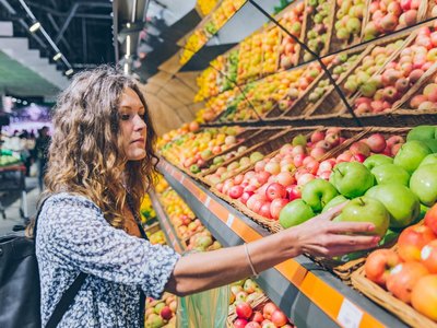 Frau am Supermarktregal mit verschiedenen Apfelsorten