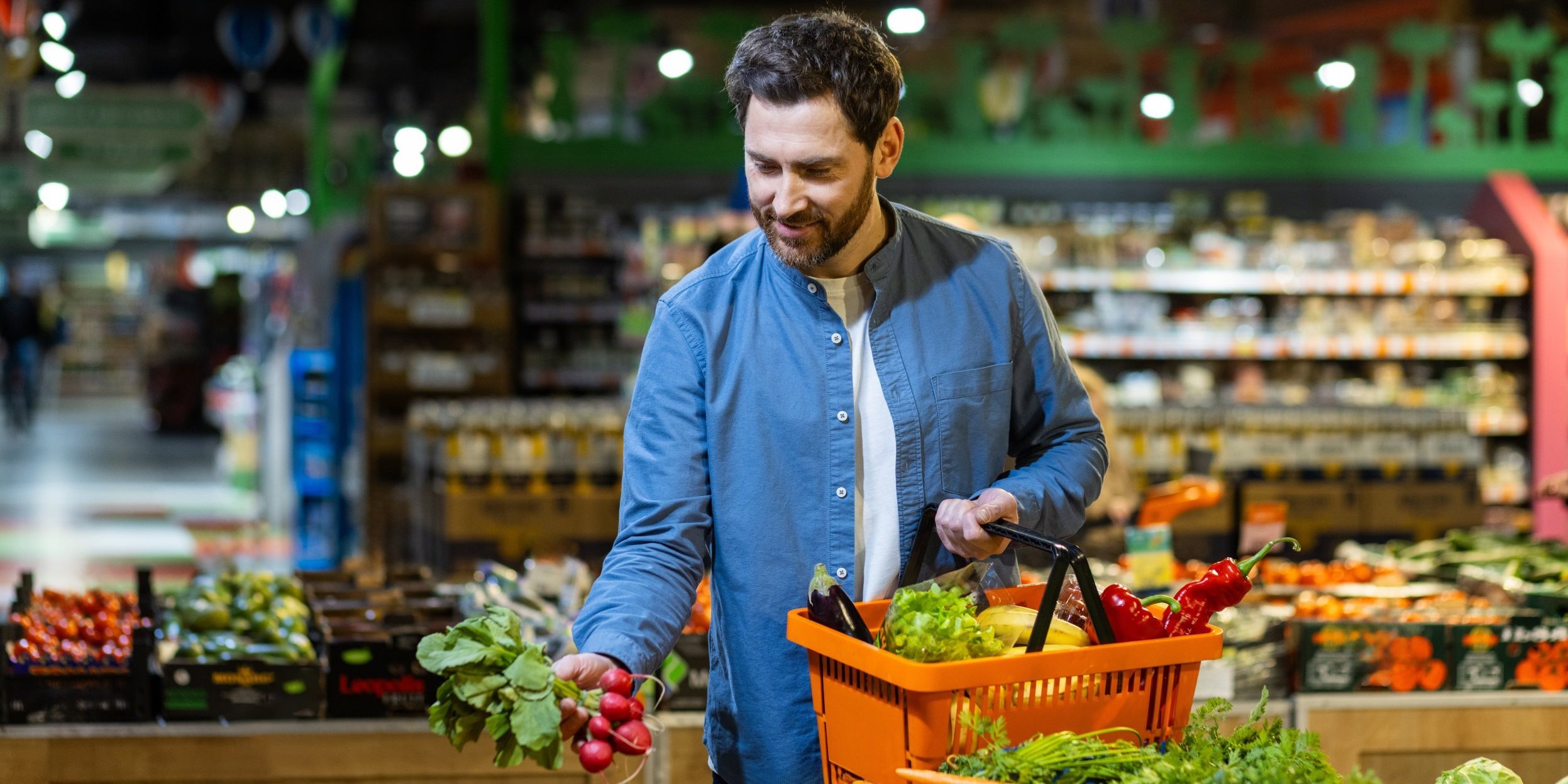 Ein Mann sucht Gemüse an der Gemüsetheke im Supermarkt aus. . Artikel "Einkaufen" öffnen.