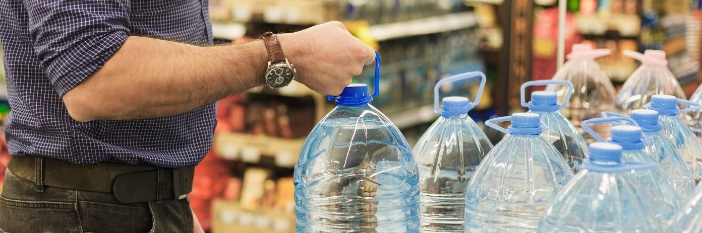 Ein Mann kauft im Supermarkt mehrere fünf-Liter-Wasserflaschen.