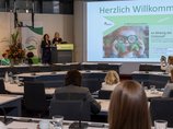 Dr. Kiran Virmani und Eva Zovko stehen am Rednerpult neben der Leinwand.