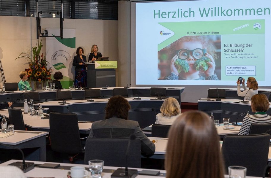 Dr. Kiran Virmani und Eva Zovko stehen am Rednerpult neben der Leinwand.