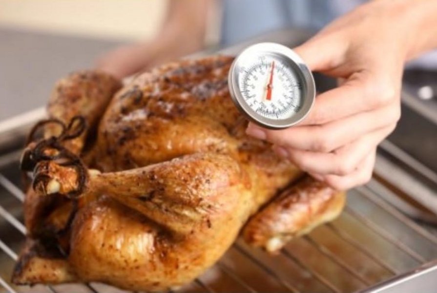 Eine Hand mit einem Fleischthermometer zeigt die Temperatur eines Brathähnchens. 
