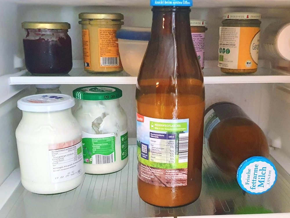 In mittleren Fach eines offenen Kühlschranks befinden sich zwei Milchflaschen und weitere Lebensmittel.