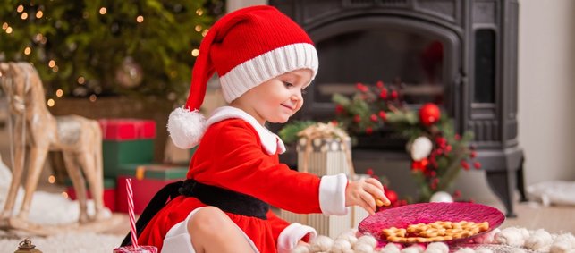 kleines Kind mit roter Weihnachtsmütze greift nach Plätzchen
