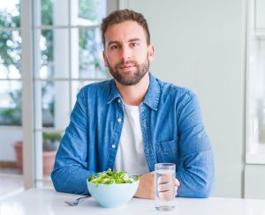 Mann sitzt vor Salat und Glas Wasser