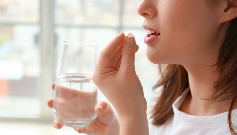 Frau führt Tablette in den Mund und hält ein Glas mit Wasser in der Hand