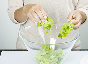 Person gibt Salatblätter in Glasschüssel