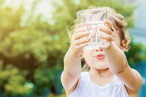 Bild: Ein kleines Kind hält ein Glas mit Wasser in den Händen.
