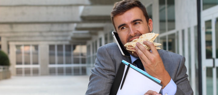 Bild: Ein Mann isst ein Brötchen. Gleichzeitig telefoniert er.