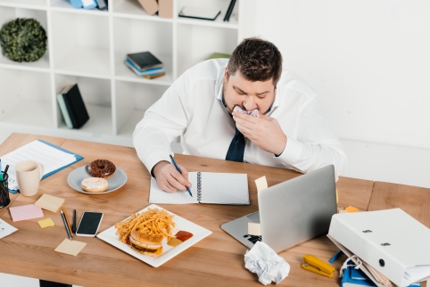 Bild: Ein Mann sitzt am Schreibtisch und isst beim Arbeiten.