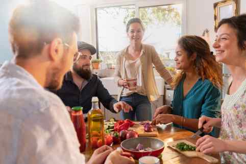 Fünf junge Leute bereiten mit Spaß am Küchentisch Speisen vor.