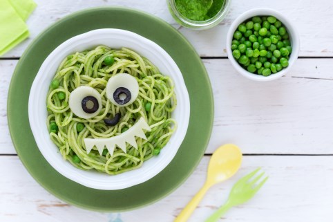 Gemüsestücke und Oliven auf einem Teller mit Spaghetti und Erbsen formen ein Gesicht