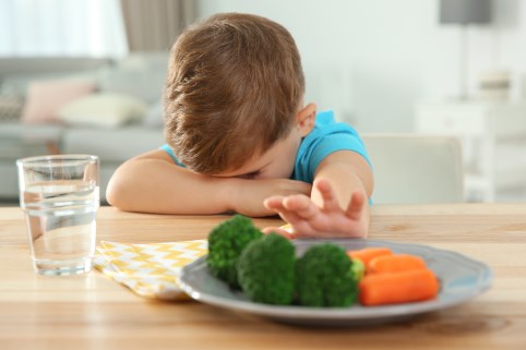 Ein Junge verdeckt sein Gesicht und schiebt einen Gemüseteller weg.